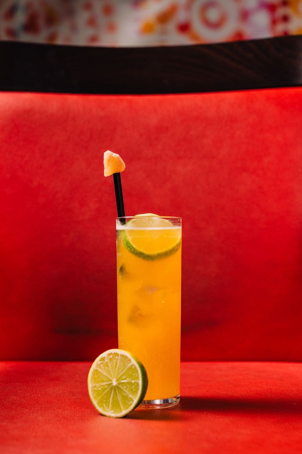 A tall orange cocktail against a red booth