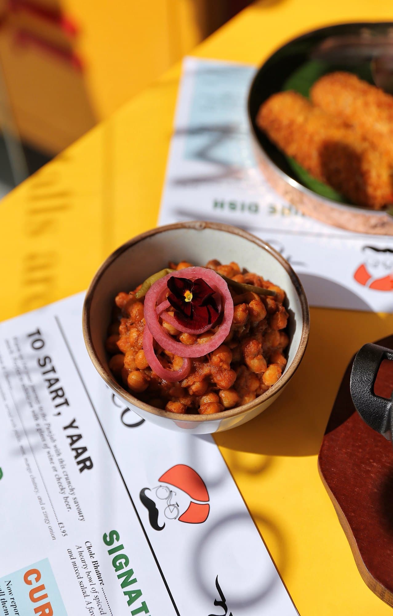 Menu, chaat and cutlery on a yellow table